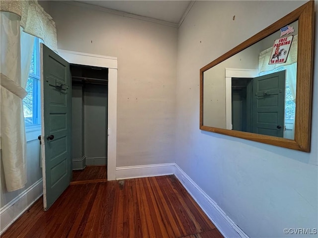 empty room with crown molding, wood finished floors, and baseboards