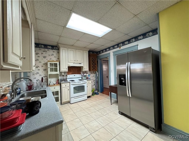 kitchen featuring under cabinet range hood, a sink, white range with electric stovetop, stainless steel fridge, and wallpapered walls