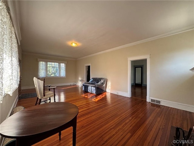 sitting room with wood-type flooring, visible vents, crown molding, and baseboards