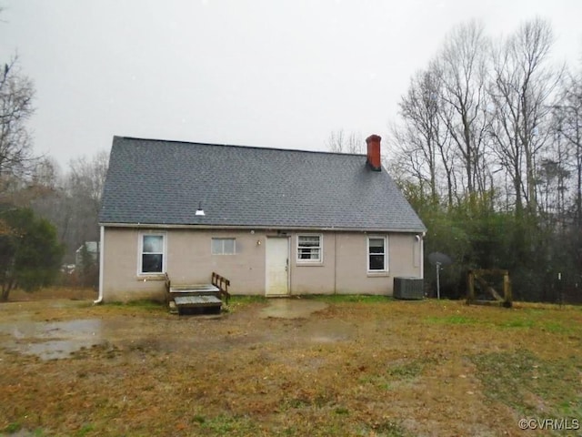 back of property featuring roof with shingles, central AC unit, and a chimney