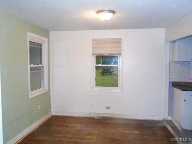 unfurnished dining area featuring dark wood finished floors and baseboards