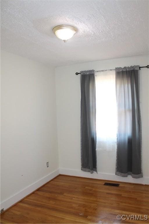 unfurnished room featuring baseboards, visible vents, wood finished floors, and a textured ceiling