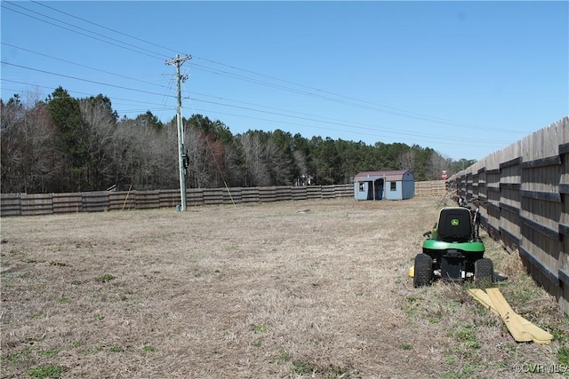 view of yard featuring a storage shed, an outbuilding, fence, and a wooded view