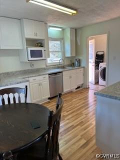 kitchen with stainless steel dishwasher, washer / clothes dryer, white cabinets, light wood-style floors, and white microwave