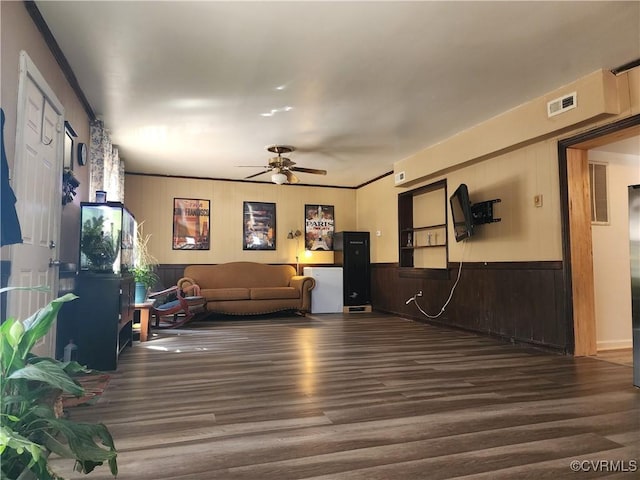 living room with a ceiling fan, a wainscoted wall, visible vents, and wood finished floors