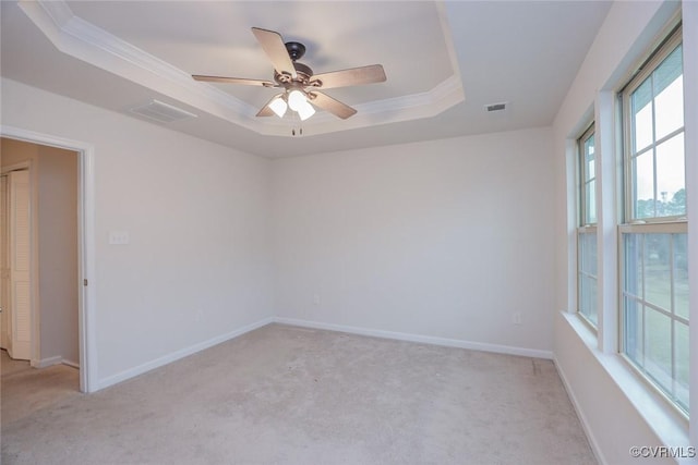 empty room featuring baseboards, visible vents, a raised ceiling, light colored carpet, and crown molding