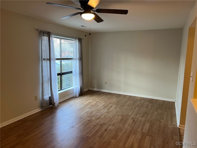 unfurnished room with a ceiling fan, visible vents, baseboards, and wood finished floors