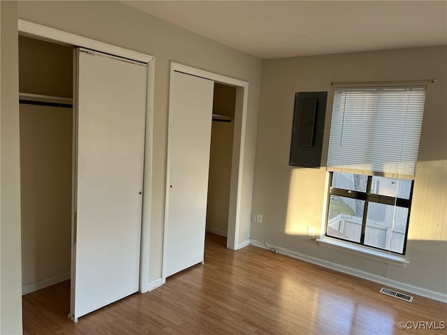 unfurnished bedroom with electric panel, baseboards, visible vents, wood finished floors, and multiple closets