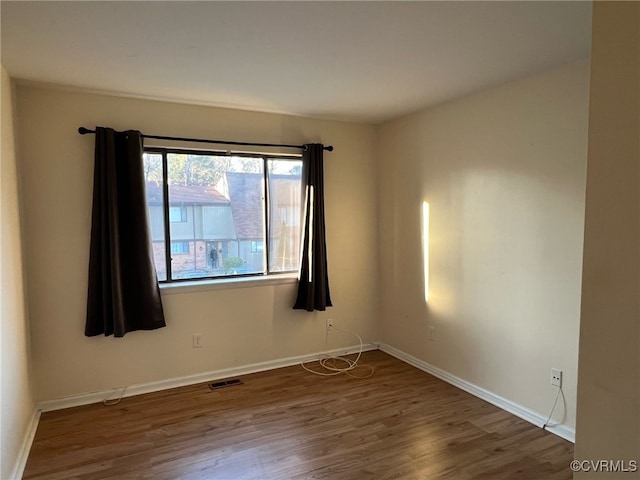 spare room with wood finished floors, visible vents, and baseboards