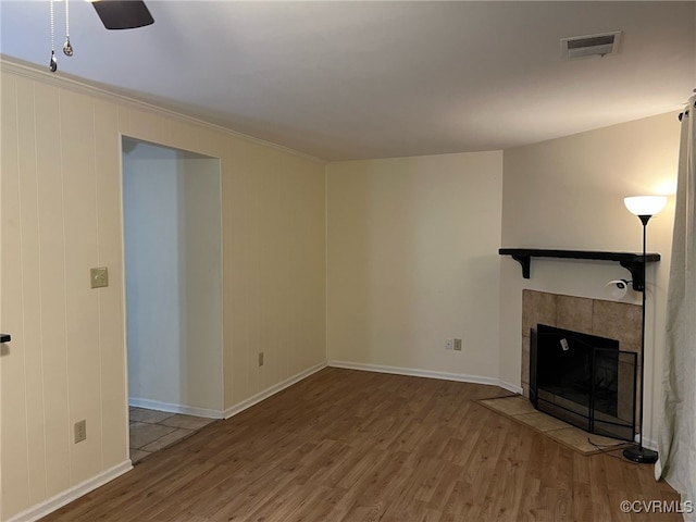 unfurnished living room with wood finished floors, a tile fireplace, visible vents, and baseboards