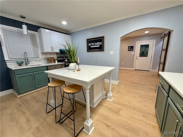 kitchen featuring light wood finished floors, arched walkways, stainless steel microwave, green cabinets, and a sink