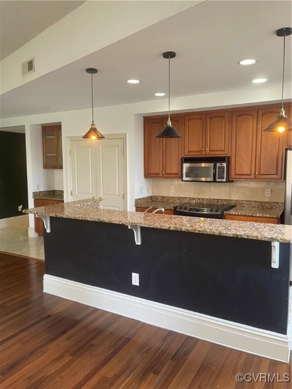 kitchen featuring electric stove, stainless steel microwave, a breakfast bar area, and visible vents