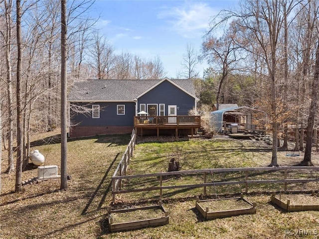 back of house featuring a lawn, a wooden deck, a vegetable garden, and a shingled roof