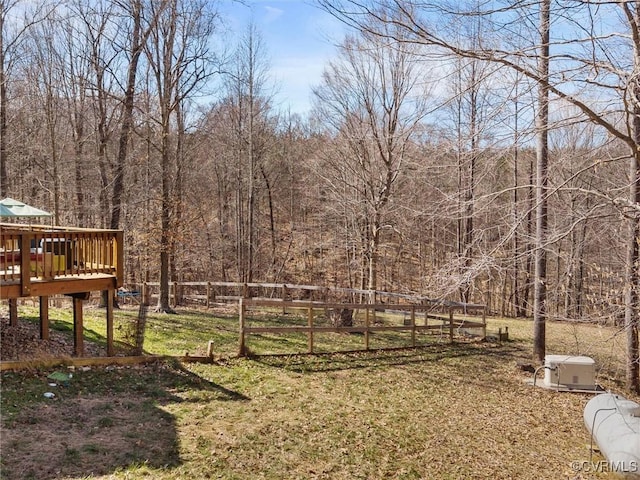 view of yard featuring fence, a wooded view, and a wooden deck