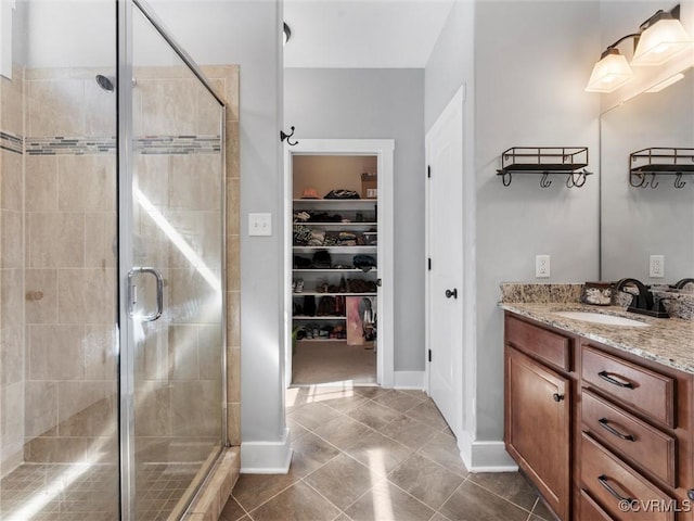 bathroom featuring vanity, baseboards, tile patterned flooring, a shower stall, and a walk in closet