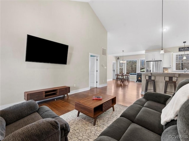 living room featuring visible vents, baseboards, wood finished floors, a notable chandelier, and high vaulted ceiling