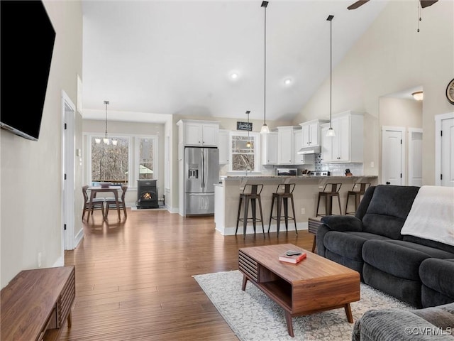 living area with ceiling fan with notable chandelier, high vaulted ceiling, baseboards, and wood finished floors