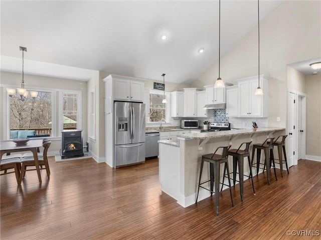 kitchen featuring a peninsula, a sink, stainless steel appliances, under cabinet range hood, and white cabinetry