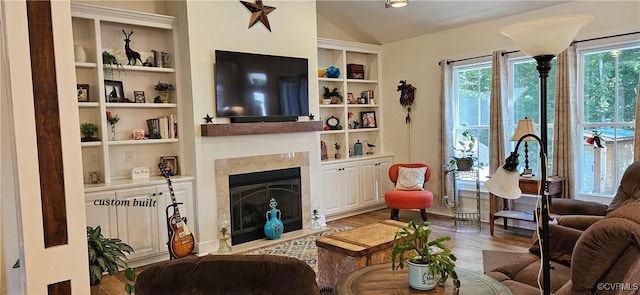 living room featuring lofted ceiling, a fireplace with flush hearth, wood finished floors, and built in shelves