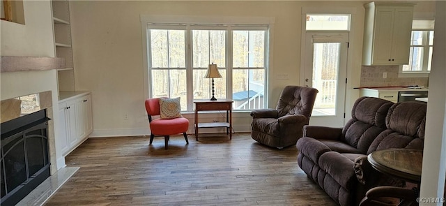 living room featuring a fireplace with flush hearth, baseboards, and dark wood-style flooring