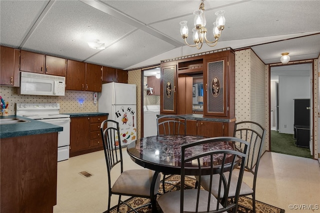 kitchen with dark countertops, a chandelier, light floors, vaulted ceiling, and white appliances