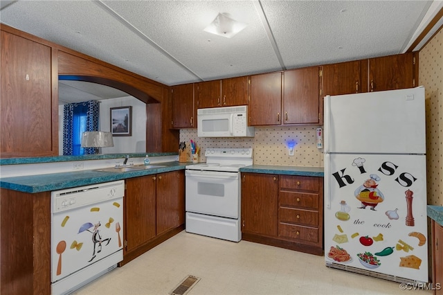 kitchen with white appliances, light floors, visible vents, a sink, and brown cabinets