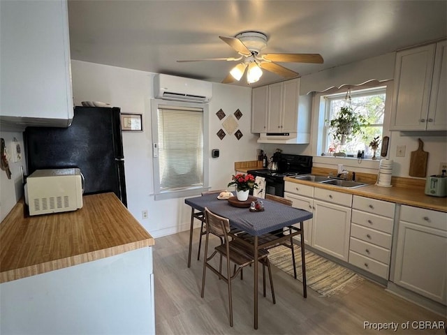 kitchen featuring light wood-style flooring, a sink, a ceiling fan, black appliances, and a wall mounted air conditioner