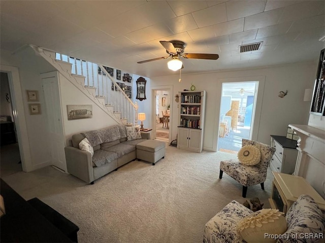 carpeted living room with stairs, ceiling fan, and visible vents