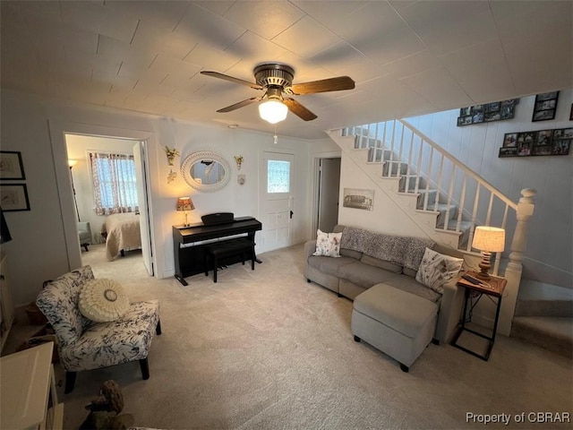 carpeted living area with stairs and a ceiling fan