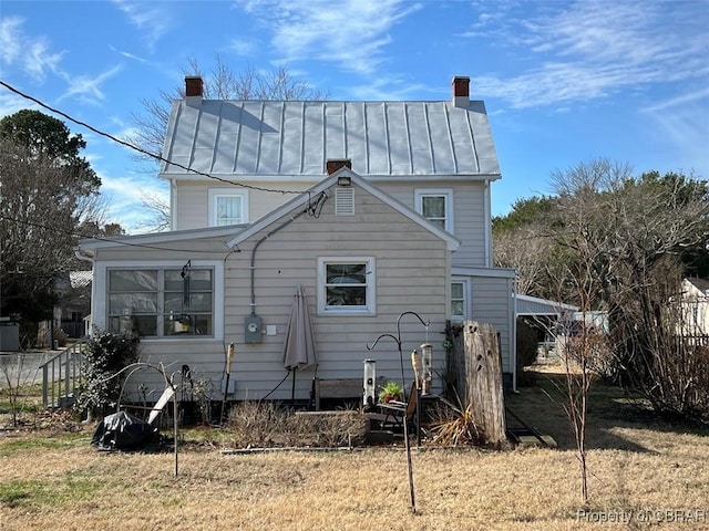 rear view of house with a standing seam roof, metal roof, a chimney, and fence