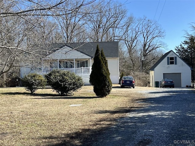 view of side of home featuring a lawn, a detached garage, gravel driveway, an outdoor structure, and a porch