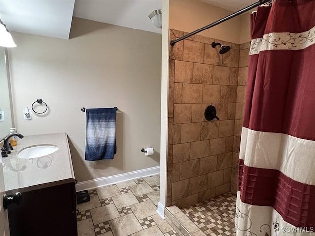 bathroom with a tile shower, vanity, and baseboards