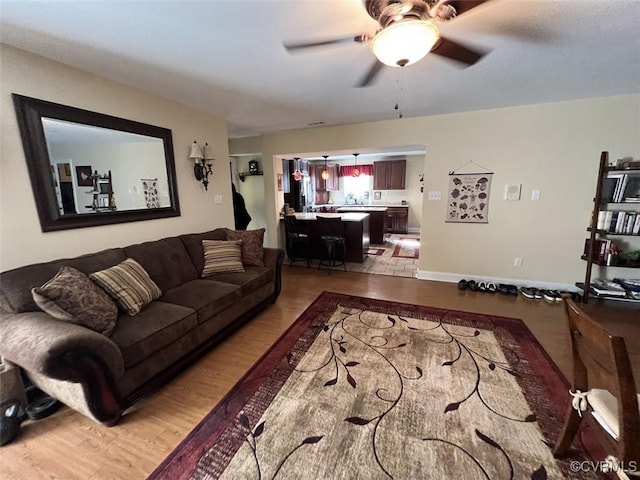 living room with light wood finished floors, ceiling fan, and baseboards