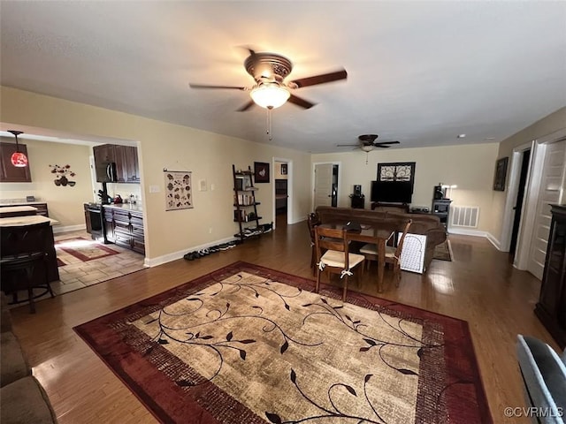 living room featuring a ceiling fan, wood finished floors, visible vents, and baseboards