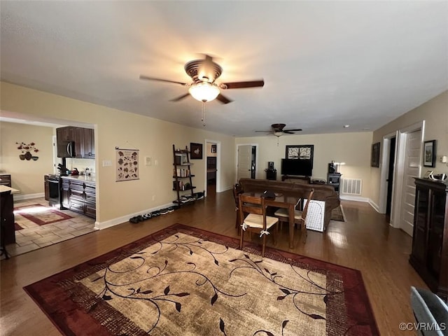 living room with ceiling fan, wood finished floors, visible vents, and baseboards