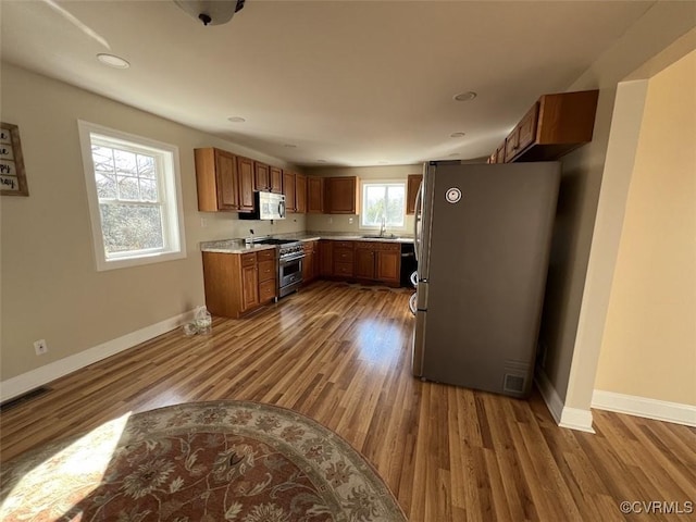 kitchen with baseboards, appliances with stainless steel finishes, brown cabinets, wood finished floors, and a sink