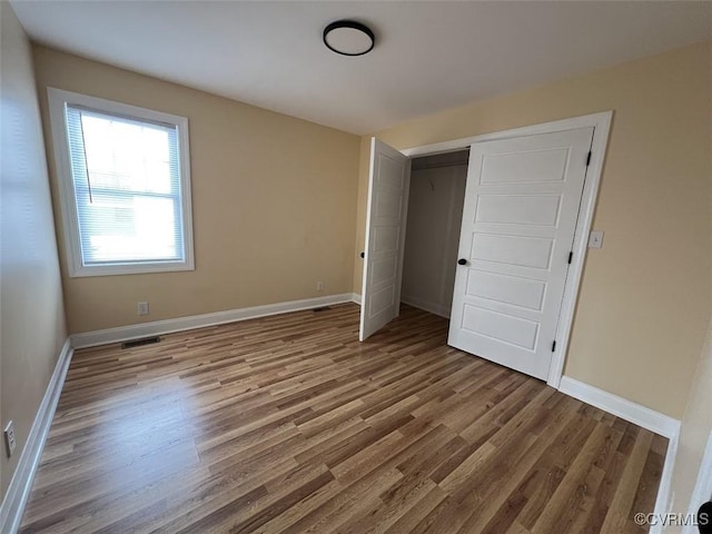 unfurnished bedroom with a closet, wood finished floors, visible vents, and baseboards