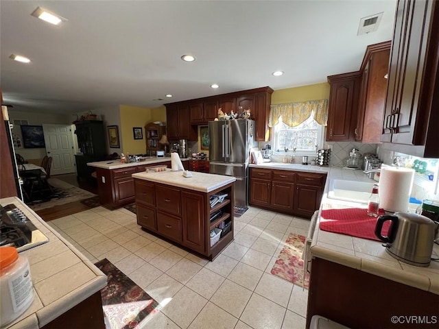 kitchen with recessed lighting, backsplash, freestanding refrigerator, light tile patterned flooring, and a sink