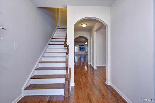 stairway with arched walkways, baseboards, and wood finished floors