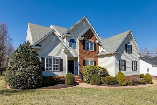 traditional home with a shingled roof, a front lawn, and brick siding