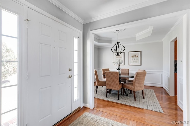 foyer entrance featuring a raised ceiling, a decorative wall, ornamental molding, wainscoting, and wood finished floors