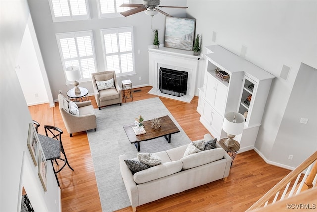 living area with baseboards, a ceiling fan, a fireplace with flush hearth, wood finished floors, and a high ceiling