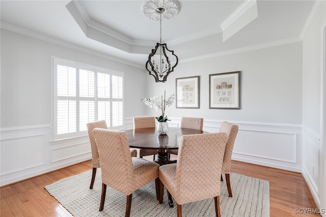 dining area with light wood-style floors, a raised ceiling, a notable chandelier, and ornamental molding