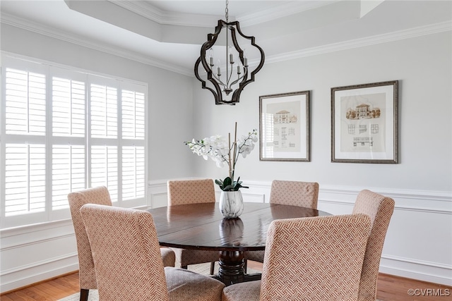 dining space featuring a tray ceiling, wainscoting, wood finished floors, and crown molding