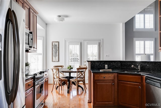 kitchen featuring stainless steel appliances, brown cabinetry, dark stone counters, a sink, and light wood-type flooring