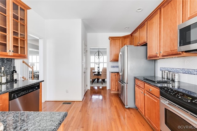 kitchen featuring appliances with stainless steel finishes, dark stone countertops, glass insert cabinets, and light wood-style floors