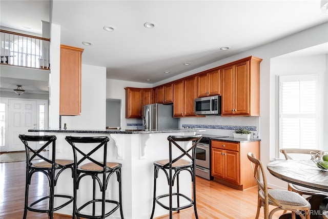 kitchen featuring dark stone counters, stainless steel appliances, light wood-type flooring, a kitchen bar, and backsplash