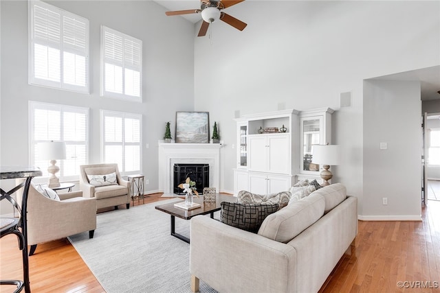 living area with a high ceiling, a fireplace, wood finished floors, visible vents, and baseboards