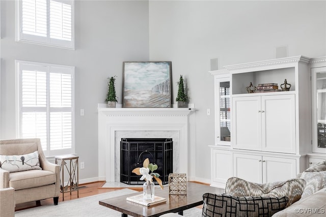 living room featuring a fireplace with flush hearth, a high ceiling, baseboards, and wood finished floors