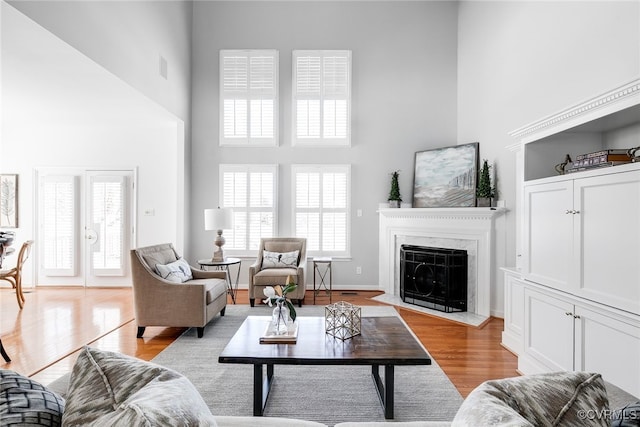 living area featuring visible vents, light wood-style flooring, a towering ceiling, a fireplace with flush hearth, and baseboards